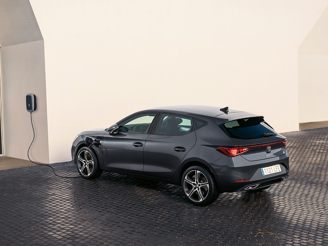 Seat leon à hayon 2025, véhicule hybride rechargeable. Garée et en train de recharger en extérieur, avec des jantes en alliage à rayons, un éclairage d’ambiance intérieur et des sièges avant chauffants pour un confort optimal.