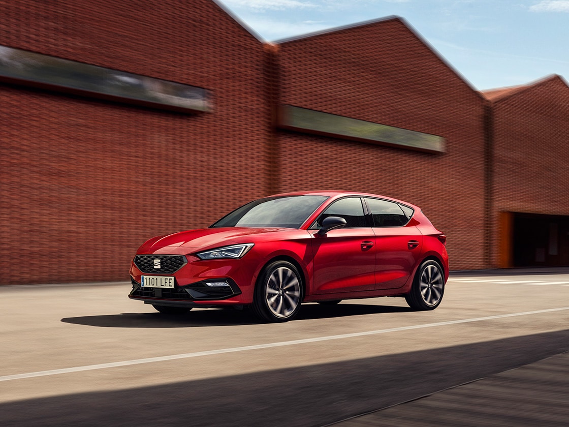 Une seat leon rouge en mouvement sur un fond industriel. Il n’y a aucune autre voiture autour, et le véhicule est impeccable, mettant en avant la fiabilité des avantages du plan de service et d’entretien de seat.