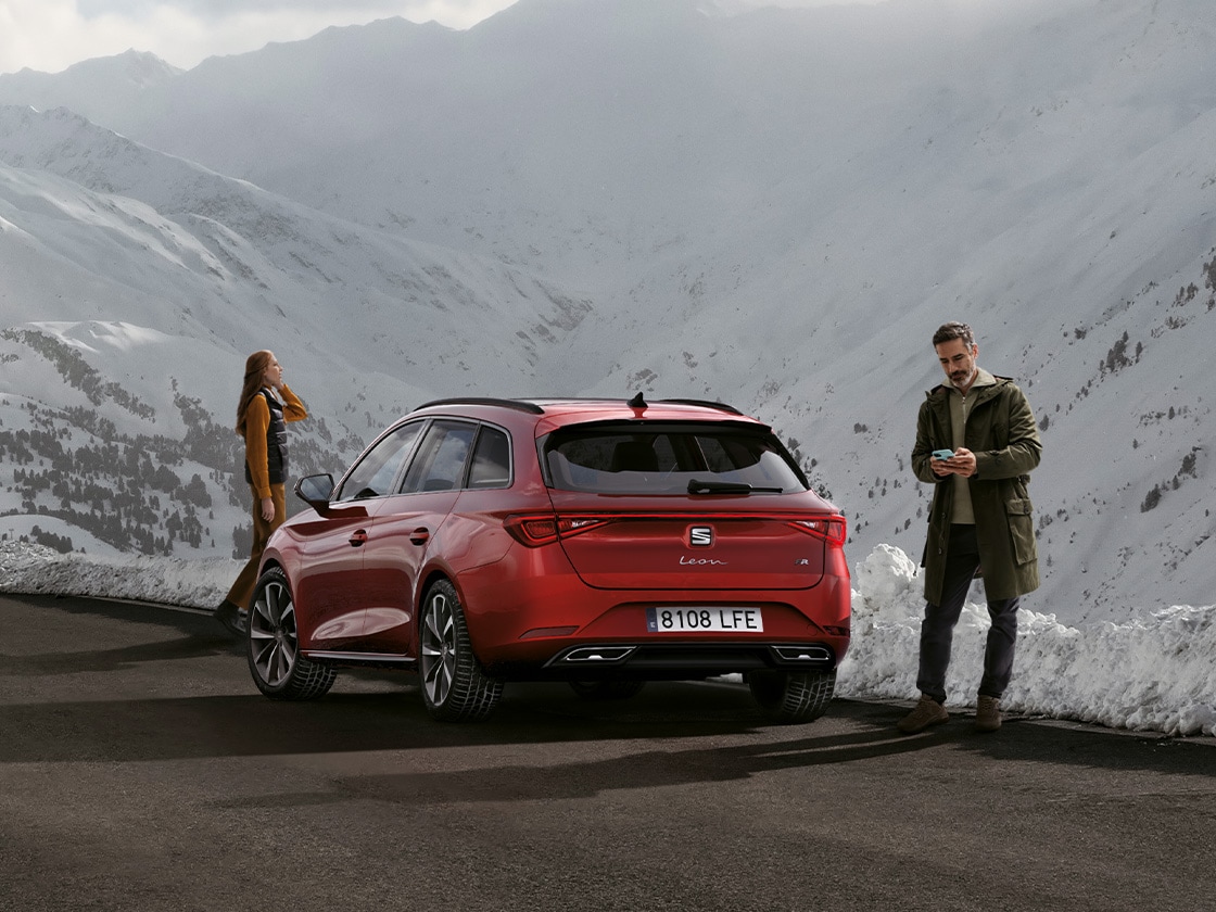 Une seat leon rouge garée sur une route de montagne, attendant les avantages du service de mobilité et de l’assistance routière seat. Deux personnes se tiennent à proximité.