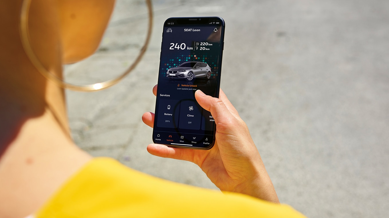 Une personne tenant un smartphone utilisant l’application my seat, une fonctionnalité de seat connect, pour l’accès à distance et les fonctionnalités du véhicule.