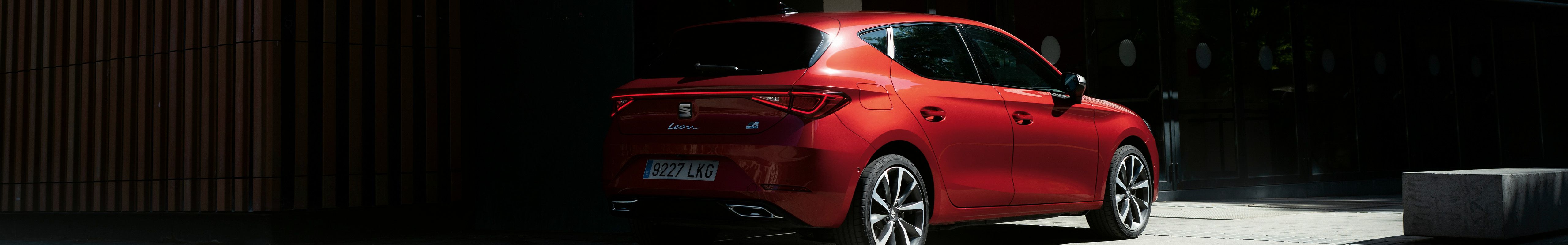 Véhicule électrique hybride léger SEAT Leon Sportstourer en rouge garé dans l'ombre près d'un bâtiment