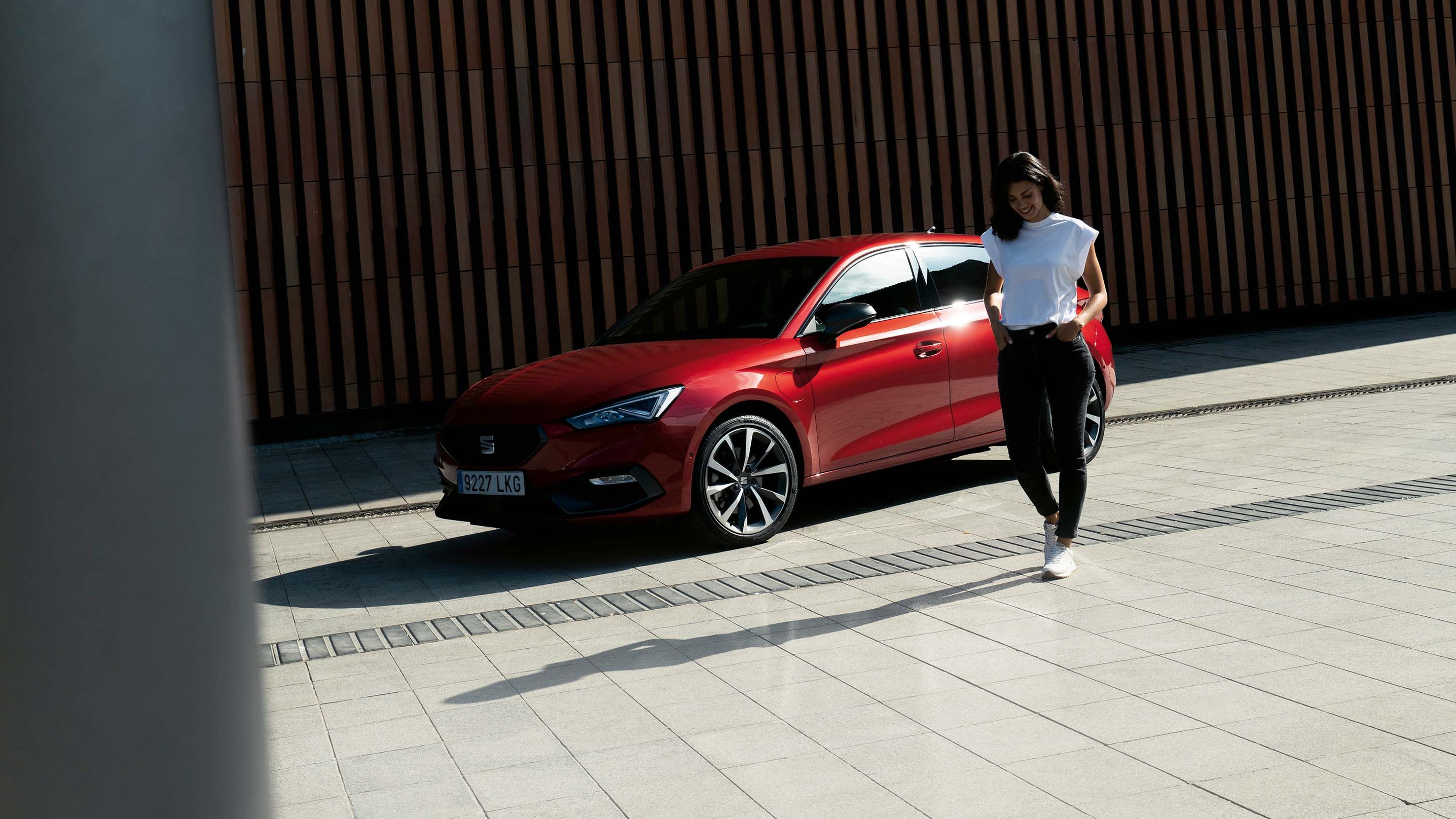 Véhicule hybride SEAT Leon rouge garé dans l'ombre près d'un bâtiment